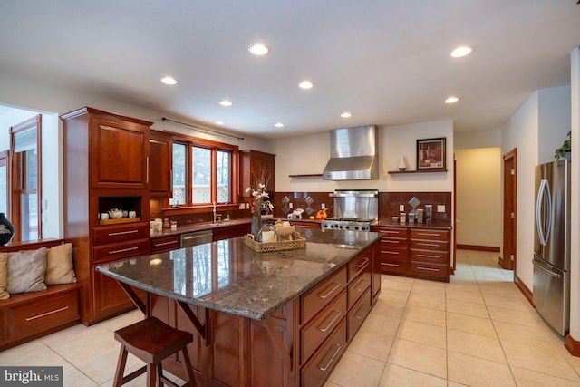 kitchen featuring light tile patterned floors, stainless steel appliances, dark stone countertops, wall chimney range hood, and a center island