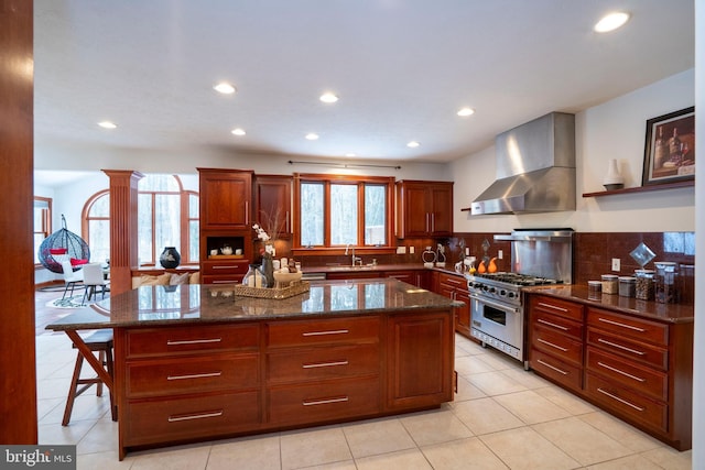 kitchen with tasteful backsplash, dark stone countertops, a center island, high end stainless steel range oven, and wall chimney exhaust hood