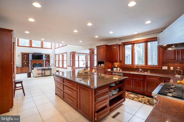 kitchen with light tile patterned floors, extractor fan, dark stone countertops, a kitchen island, and sink