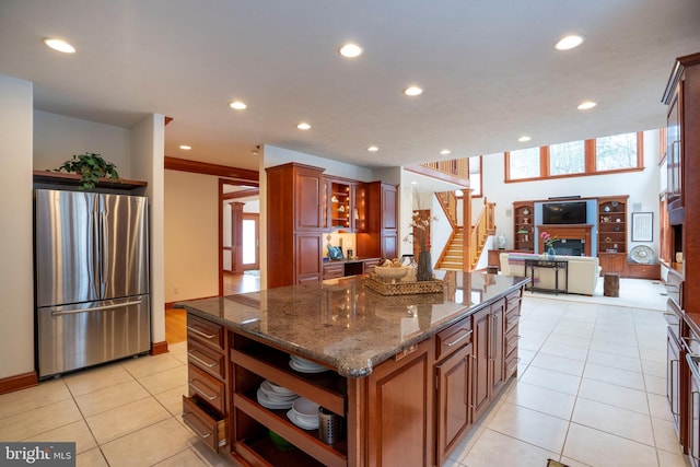 kitchen with light tile patterned flooring, a kitchen island, dark stone counters, and stainless steel refrigerator