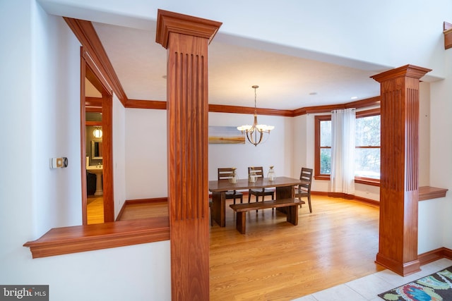 dining area featuring light wood-type flooring, a notable chandelier, crown molding, and ornate columns