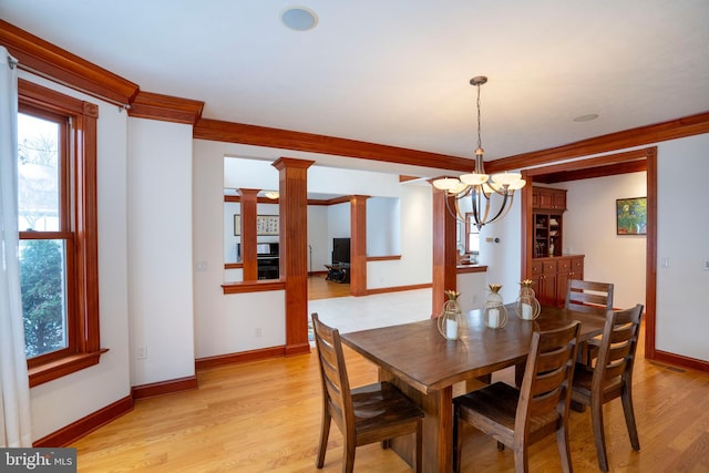 dining room featuring crown molding, ornate columns, a chandelier, and light wood-type flooring