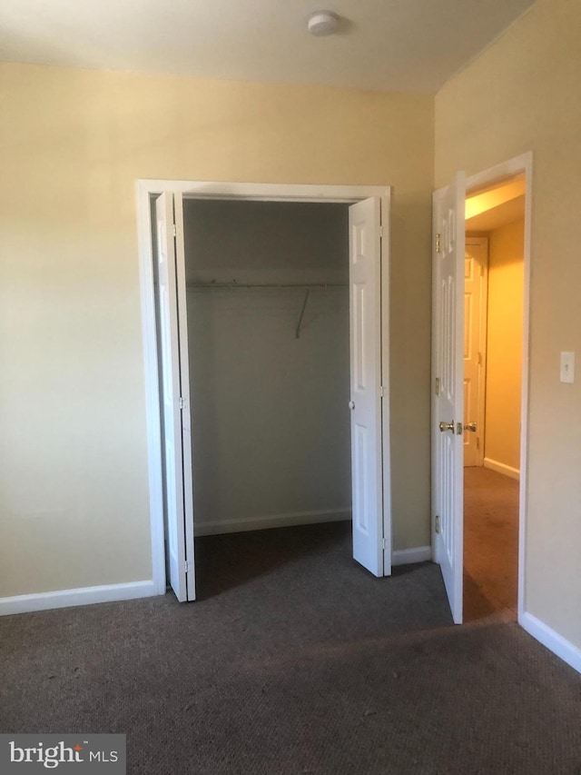 unfurnished bedroom featuring dark carpet and a closet