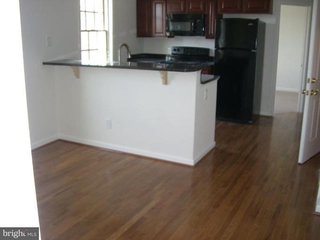 kitchen featuring dark wood-type flooring, kitchen peninsula, a kitchen bar, and black appliances