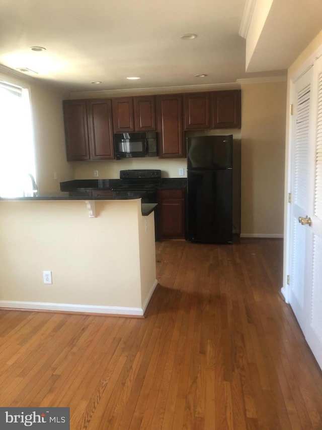 kitchen with dark hardwood / wood-style floors, black appliances, a kitchen breakfast bar, kitchen peninsula, and crown molding