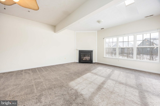 unfurnished living room with ceiling fan, carpet flooring, and beam ceiling