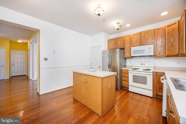 kitchen featuring sink, white appliances, a textured ceiling, a kitchen island, and light wood-type flooring