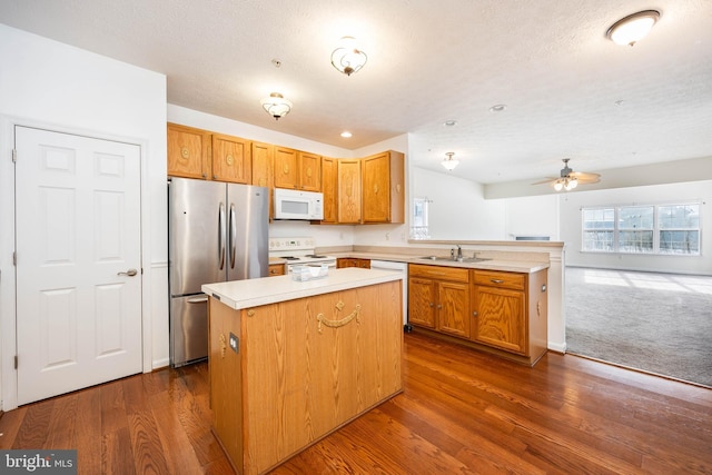 kitchen with sink, dark hardwood / wood-style flooring, a center island, white appliances, and a textured ceiling