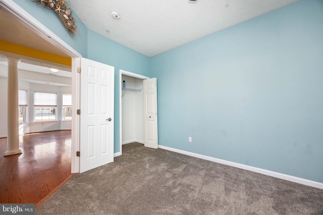 unfurnished bedroom featuring decorative columns, dark colored carpet, and a textured ceiling