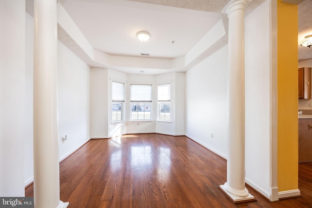 unfurnished living room with decorative columns, dark hardwood / wood-style floors, and a raised ceiling