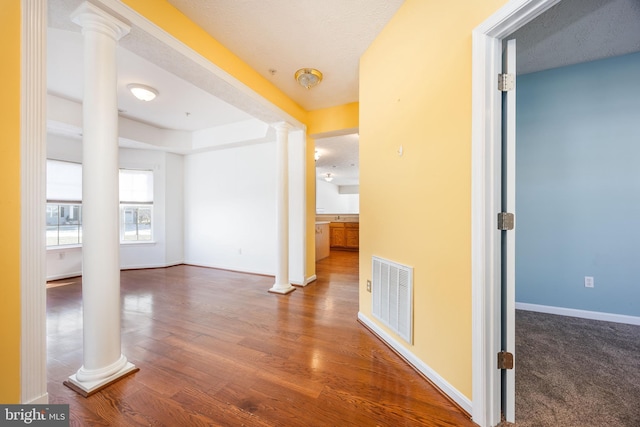 corridor featuring ornate columns, dark wood-type flooring, and a textured ceiling