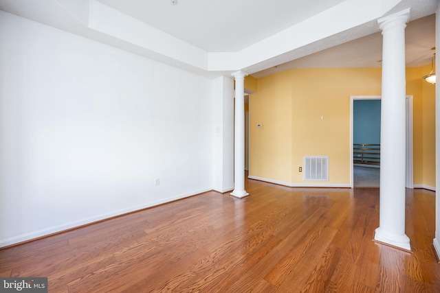 unfurnished room with a tray ceiling, wood-type flooring, and decorative columns