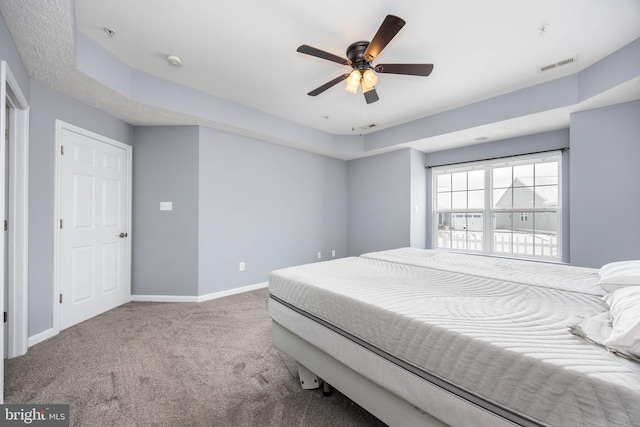 carpeted bedroom with a raised ceiling and ceiling fan