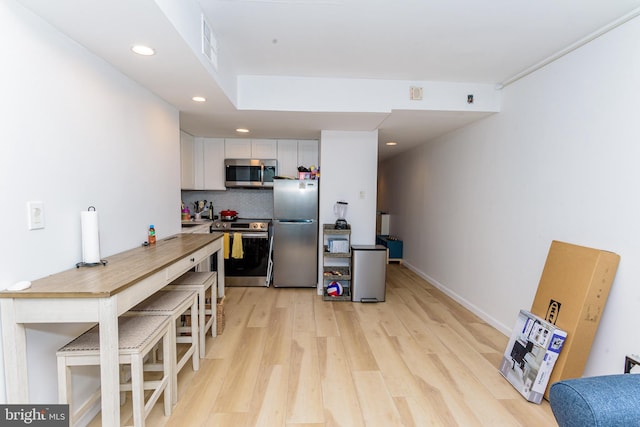 kitchen with white cabinets, stainless steel appliances, decorative backsplash, kitchen peninsula, and light hardwood / wood-style flooring