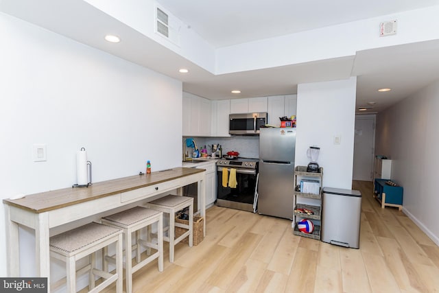 kitchen featuring white cabinetry, light hardwood / wood-style floors, a kitchen bar, appliances with stainless steel finishes, and tasteful backsplash