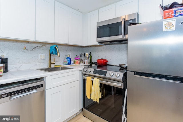 kitchen with backsplash, sink, appliances with stainless steel finishes, white cabinets, and light stone counters