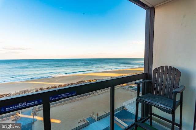 balcony at dusk with a water view and a view of the beach