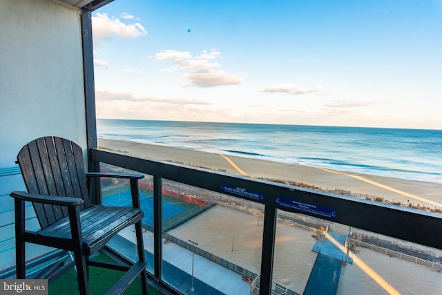 balcony at dusk featuring a view of the beach and a water view