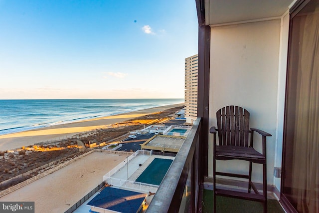 balcony at dusk featuring a water view and a beach view