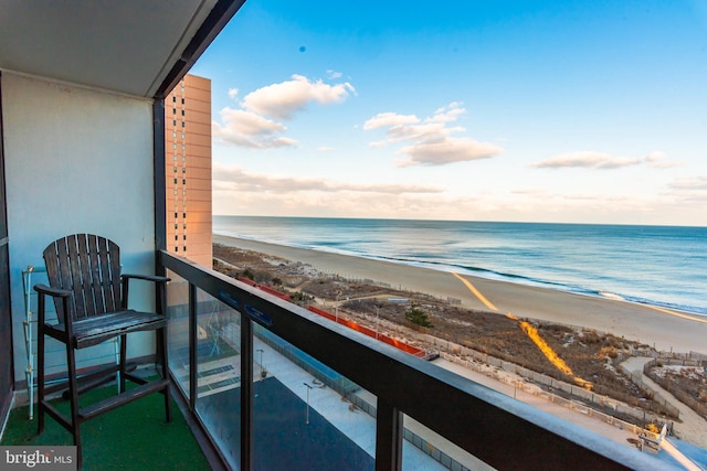 balcony at dusk featuring a water view and a beach view