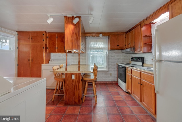 kitchen featuring track lighting, white fridge, plenty of natural light, a kitchen breakfast bar, and electric range