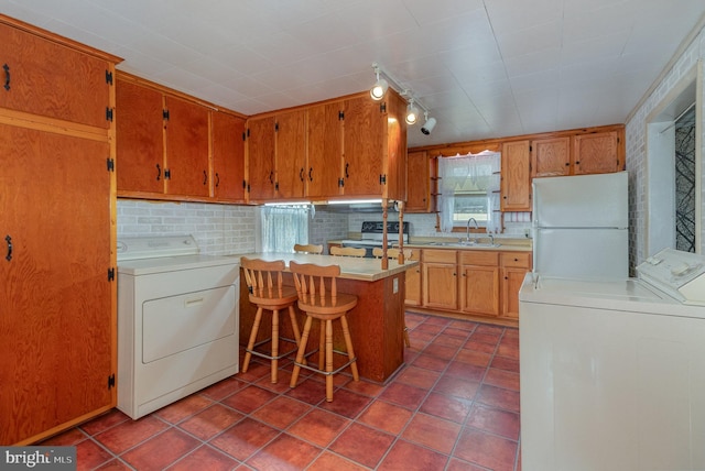 kitchen featuring washing machine and dryer, a kitchen bar, white refrigerator, rail lighting, and sink