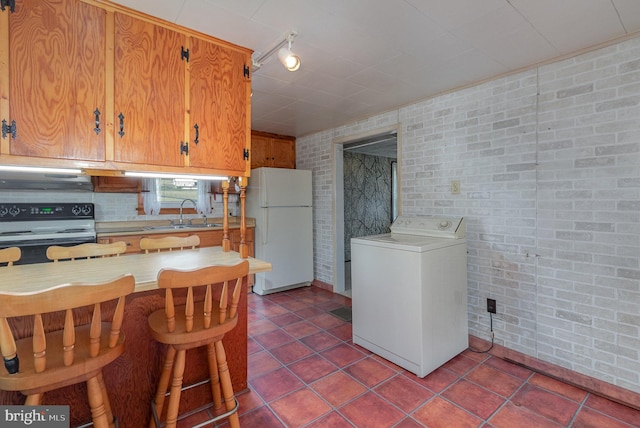 kitchen featuring electric stove, washer / dryer, sink, brick wall, and white refrigerator