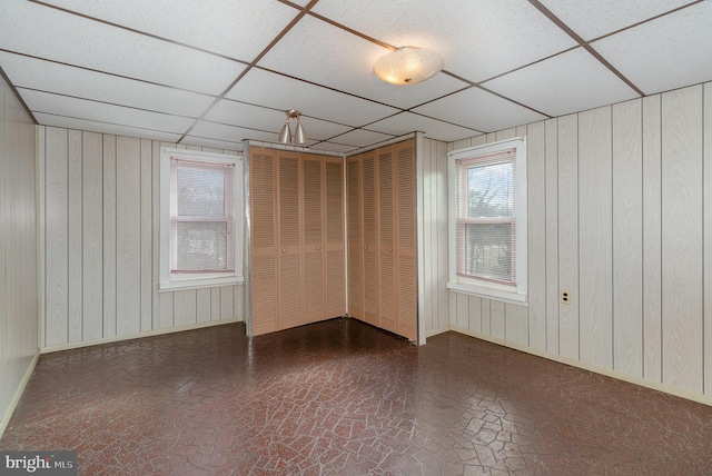 unfurnished room with a drop ceiling and wooden walls