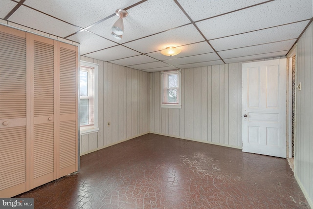 unfurnished bedroom with a closet, wood walls, and a paneled ceiling