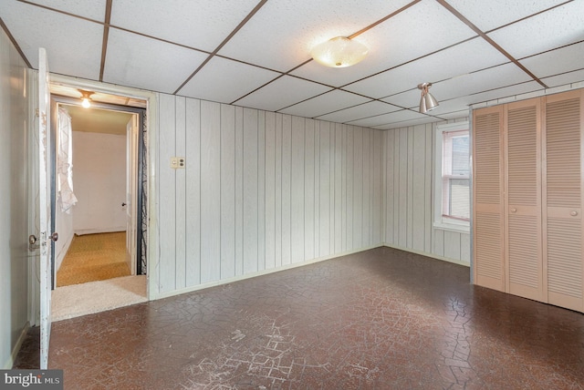 interior space with a paneled ceiling, a closet, and wooden walls