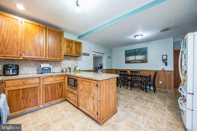 kitchen featuring stainless steel microwave, kitchen peninsula, decorative backsplash, and white fridge