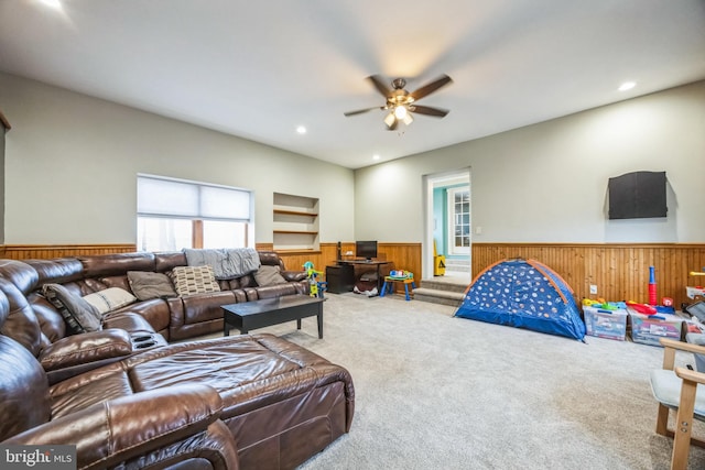 carpeted living room featuring ceiling fan and wooden walls