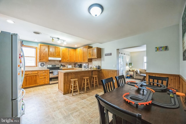 kitchen featuring refrigerator, a breakfast bar, kitchen peninsula, double oven range, and wooden walls