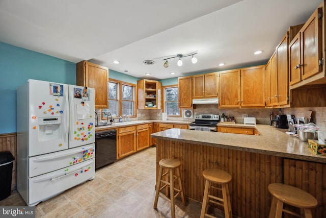 kitchen featuring electric stove, dishwasher, kitchen peninsula, white refrigerator with ice dispenser, and a breakfast bar area