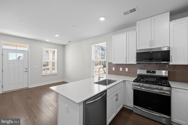 kitchen with white cabinetry, kitchen peninsula, appliances with stainless steel finishes, tasteful backsplash, and sink