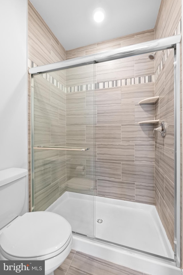 bathroom with a shower with shower door and toilet