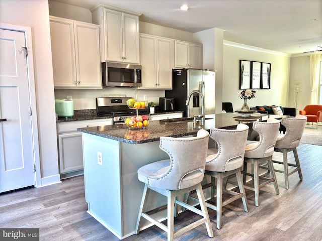 kitchen featuring light hardwood / wood-style flooring, a kitchen bar, stainless steel appliances, and a center island with sink