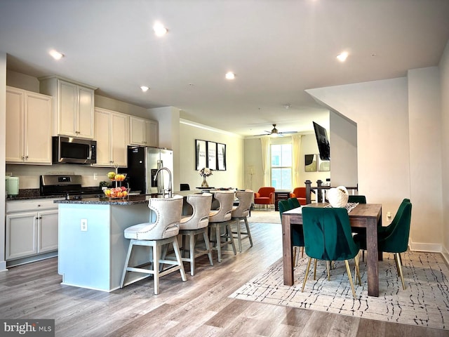 kitchen with dark stone countertops, light hardwood / wood-style floors, a kitchen island with sink, a breakfast bar area, and stainless steel appliances