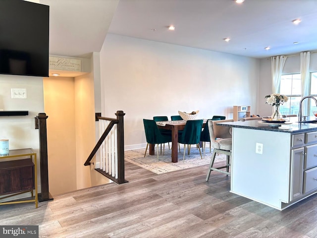 kitchen featuring dark stone counters, sink, a kitchen island with sink, light wood-type flooring, and a breakfast bar