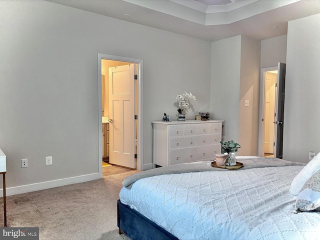 carpeted bedroom featuring a raised ceiling and connected bathroom