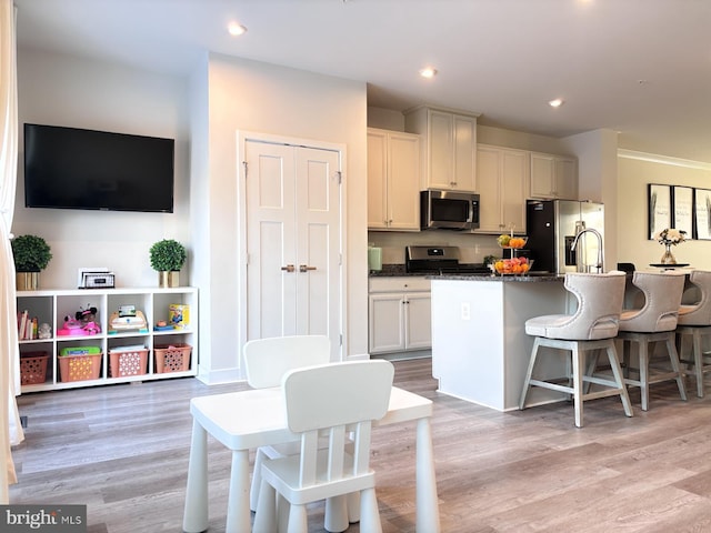 kitchen featuring stainless steel appliances, dark stone counters, a kitchen breakfast bar, a kitchen island with sink, and light hardwood / wood-style flooring