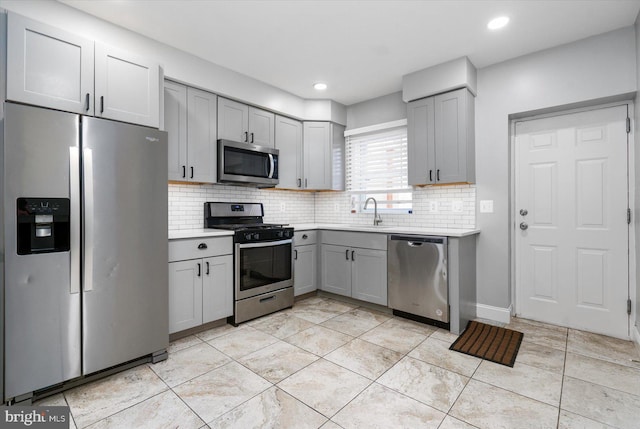 kitchen featuring appliances with stainless steel finishes, gray cabinetry, backsplash, and sink