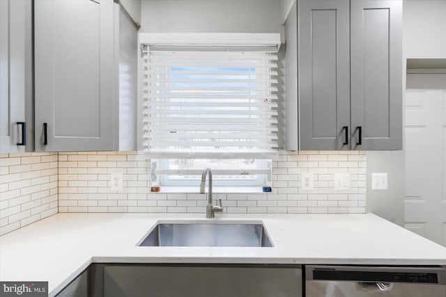 kitchen with stainless steel dishwasher, decorative backsplash, sink, and gray cabinets