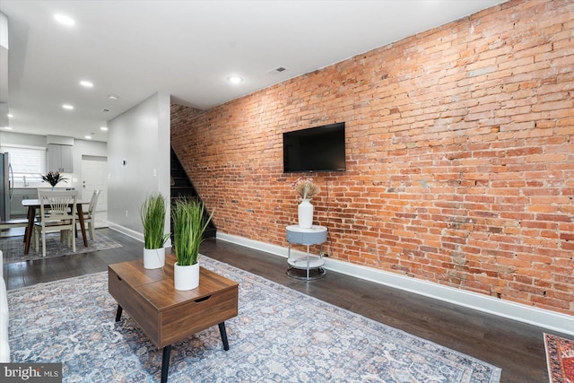 living room with dark wood-type flooring and brick wall