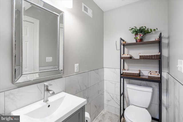 bathroom featuring toilet, vanity, and tile walls