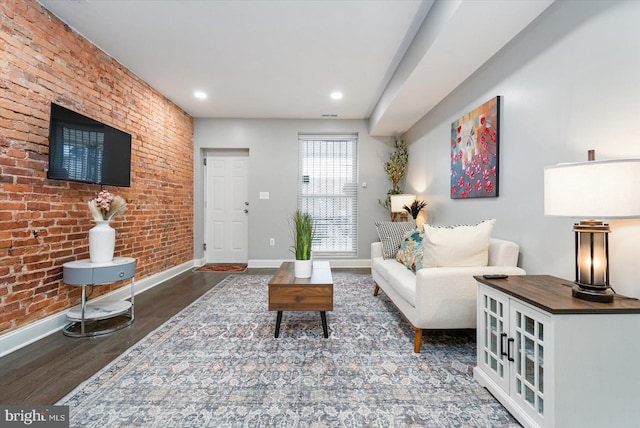 living room featuring dark wood-type flooring and brick wall