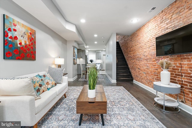 living room with brick wall and dark hardwood / wood-style flooring