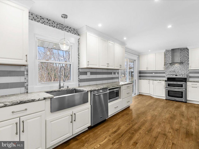 kitchen with sink, white cabinetry, appliances with stainless steel finishes, pendant lighting, and wall chimney range hood