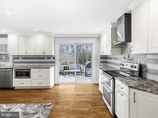 kitchen with white cabinets, appliances with stainless steel finishes, dark stone counters, and wall chimney range hood