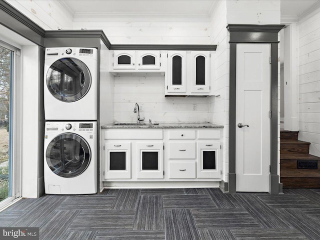 clothes washing area with stacked washer / dryer, ornamental molding, sink, and wooden walls